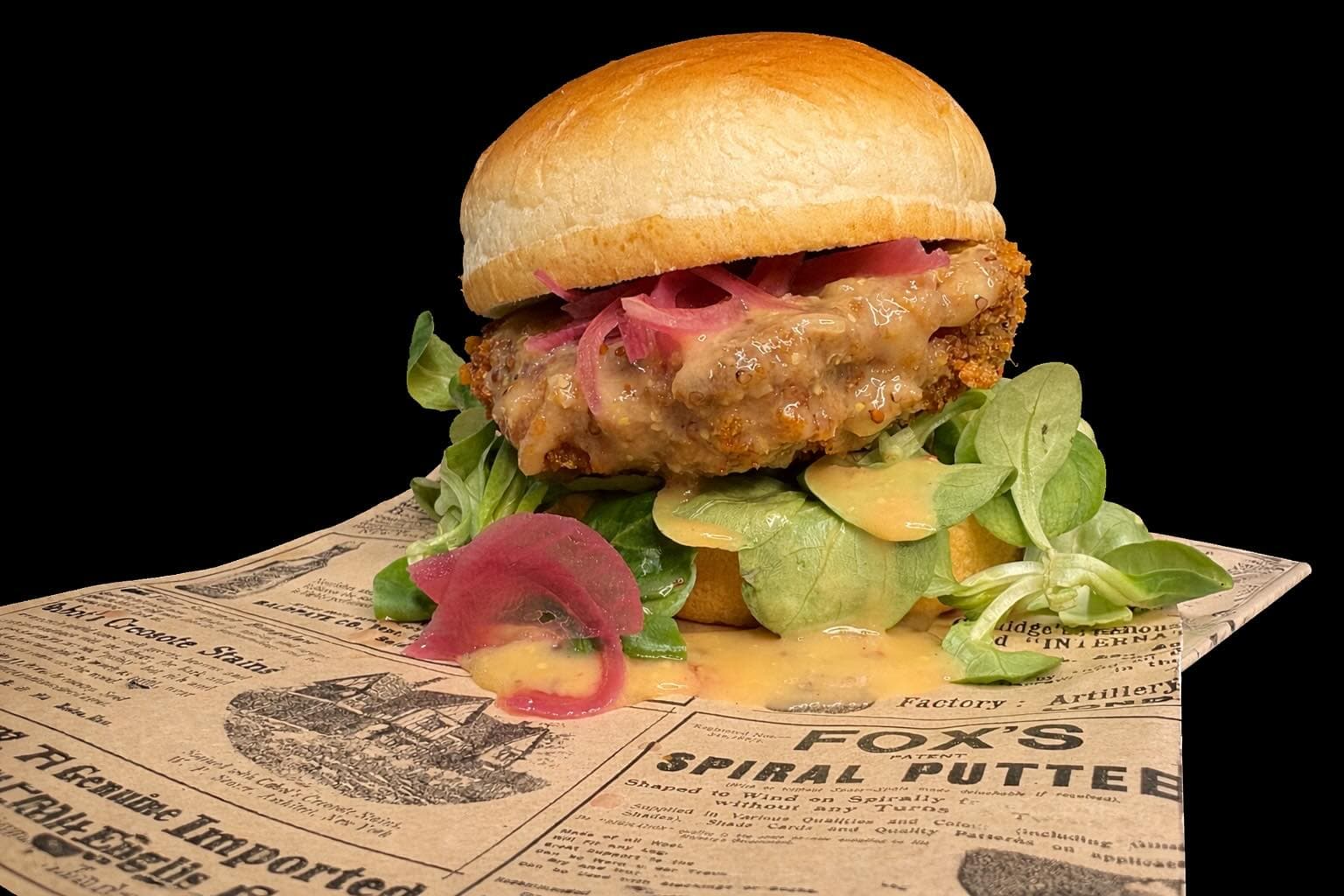 Sándwich de pollo crujiente con cebollas encurtidas y brotes sobre papel de periódico antiguo.