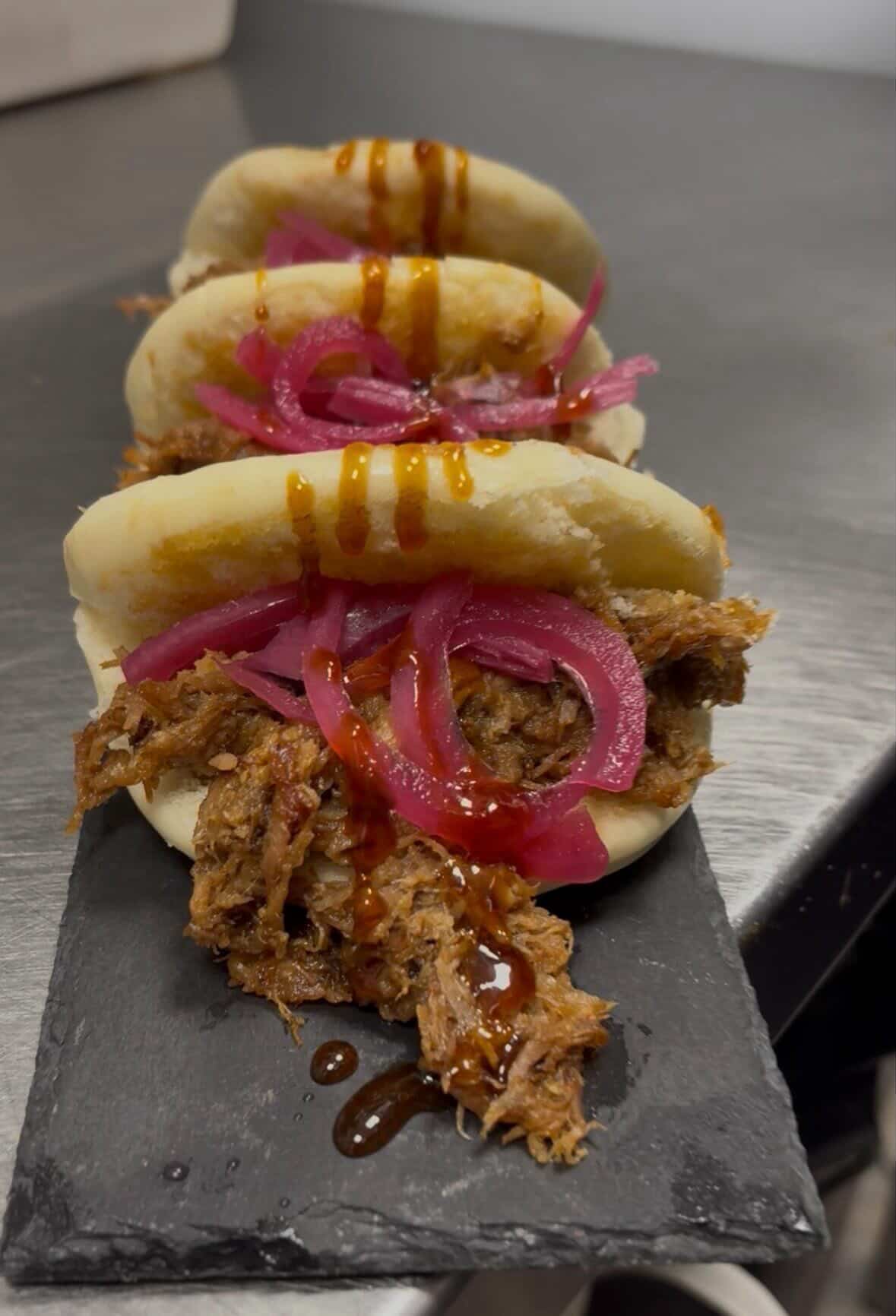Tres arepas rellenas de carne desmechada, cebolla roja encurtida y salsa sobre una tabla negra.
